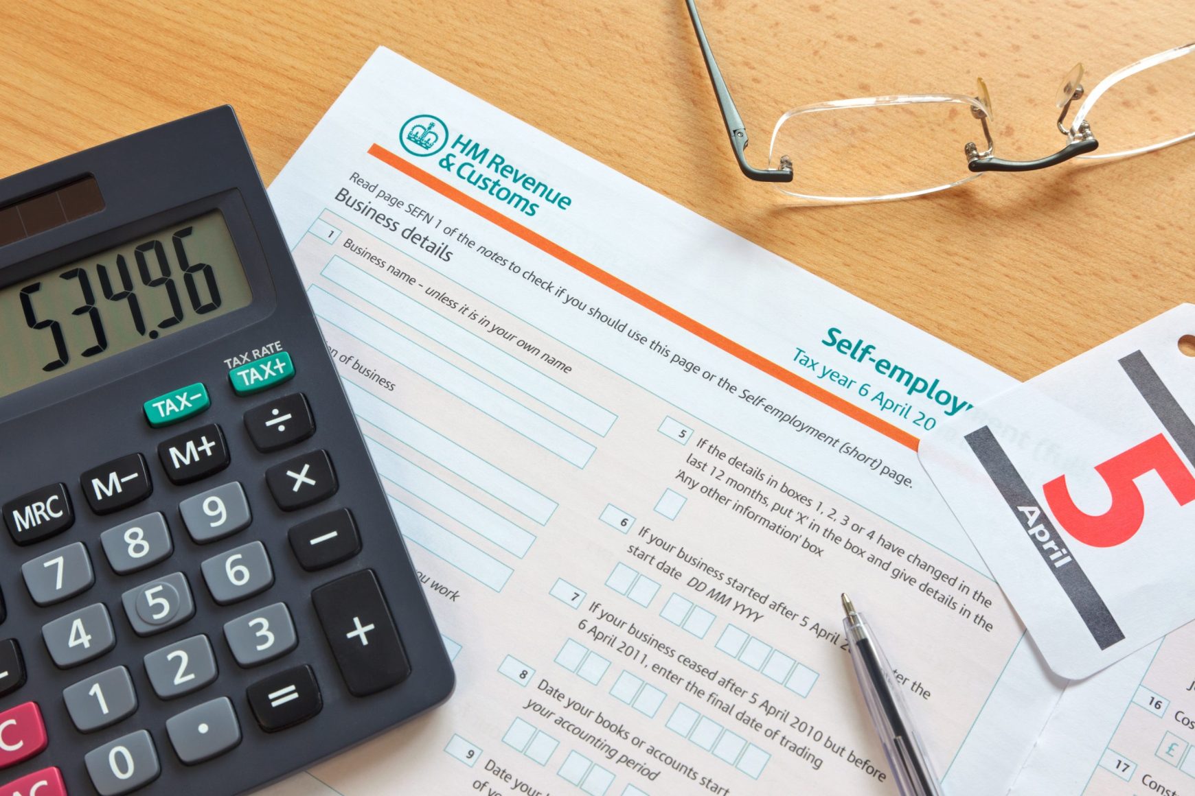 Self employment tax form on desk with calculator and reading glasses