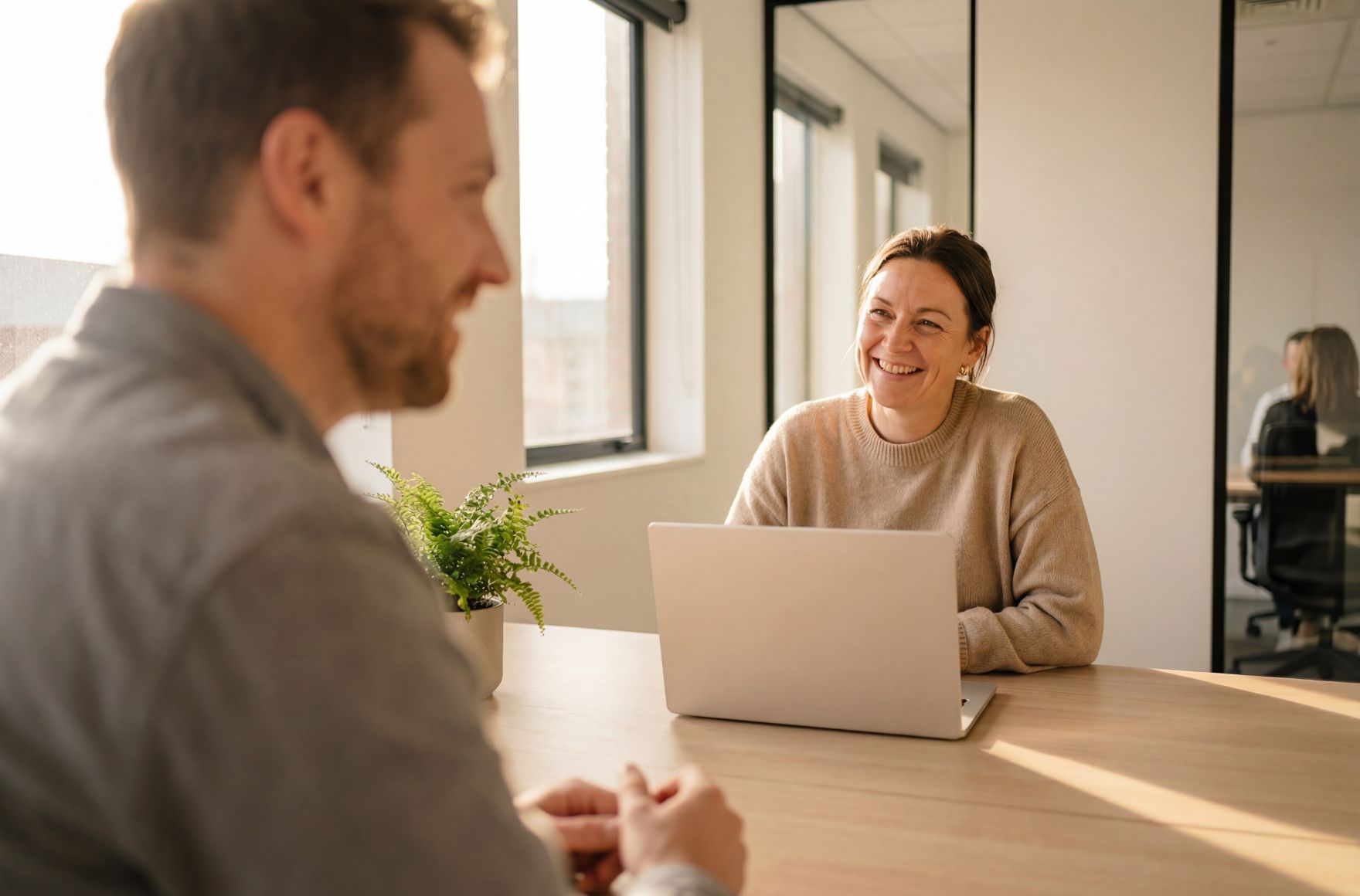 Smiling woman with laptop on table sits across from a man with a beard